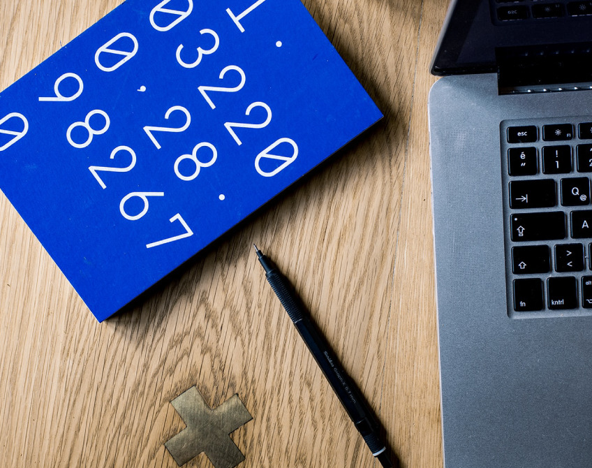 Desk setup with a laptop, pen, and a blue notebook featuring numbers