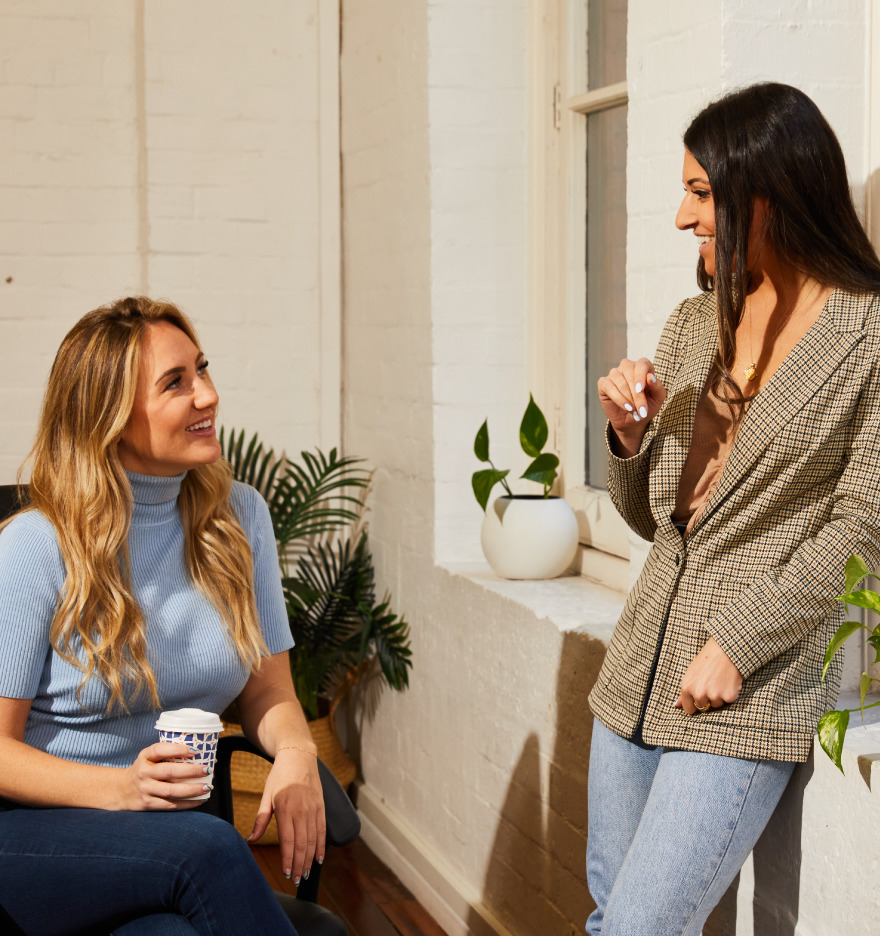 A photo of two women having a casual conversation in a bright office space