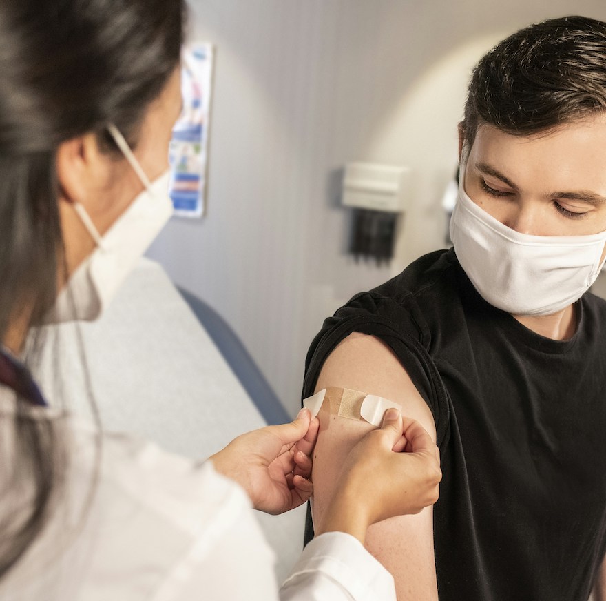 Healthcare professional applying a bandage to a patient’s arm after vaccination, both wearing face masks