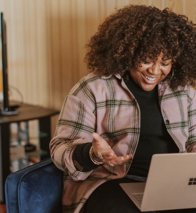 Smiling woman with curly hair facing her laptop.
