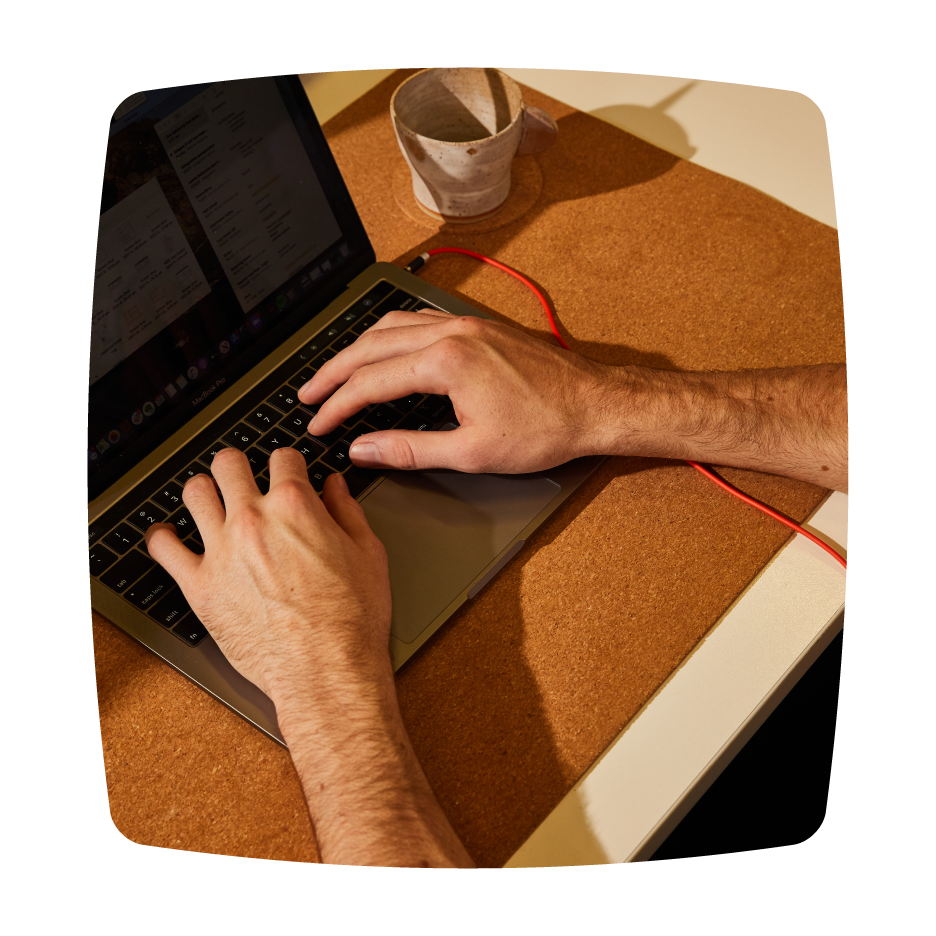 Close-up of hands typing on a laptop keyboard on a cork mat desk