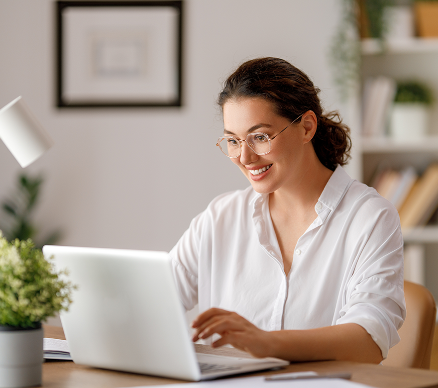 An image of a woman smiling while typing on her laptop