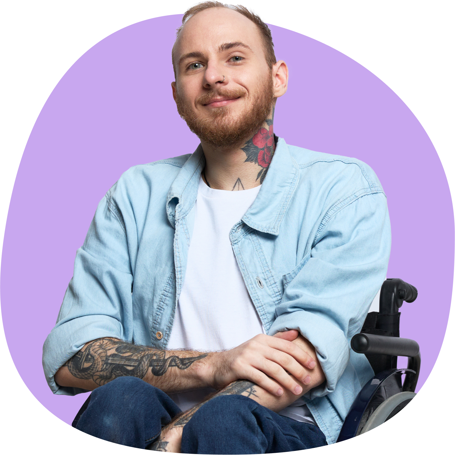 A smiling man with tattoos sitting in a wheelchair, wearing a denim shirt and white t-shirt.